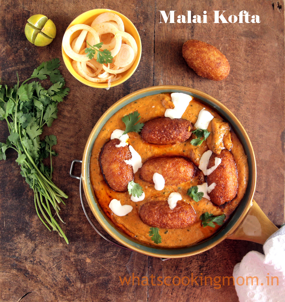 Malai Kofta served in a bowl garnished with cream and coriander leaves and onion salad